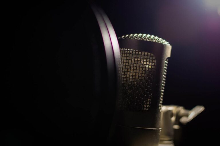 Gros plan d'un microphone avec un filtre anti-pop partiellement visible dans un environnement faiblement éclairé. Le maillage du microphone est mis en valeur par un éclairage tamisé provenant du coin supérieur droit.