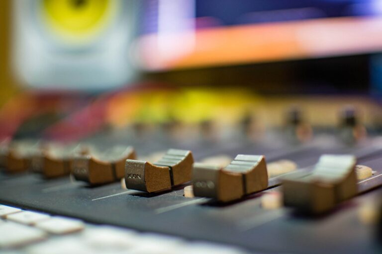 Gros plan d'une console de mixage sonore avec plusieurs curseurs dans différentes positions, sur un arrière-plan flou d'équipement audio.