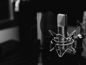 A close-up of a microphone with a pop filter in a dimly lit recording studio. The background is out of focus.