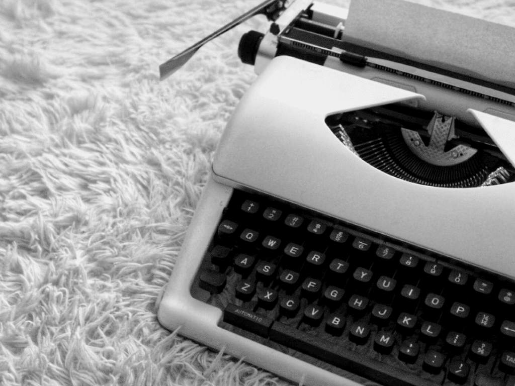 Une photo en noir et blanc d'une machine à écrire vintage sur une surface moelleuse avec une feuille de papier chargée dedans.