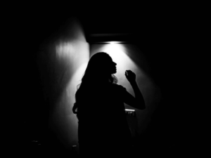 Silhouette of a woman standing in a dark room, illuminated by a single light source from behind, creating a dramatic effect.