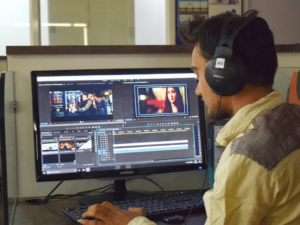 A person wearing headphones is working in a dubbing studio, meticulously editing video clips on the screen at their computer desk.
