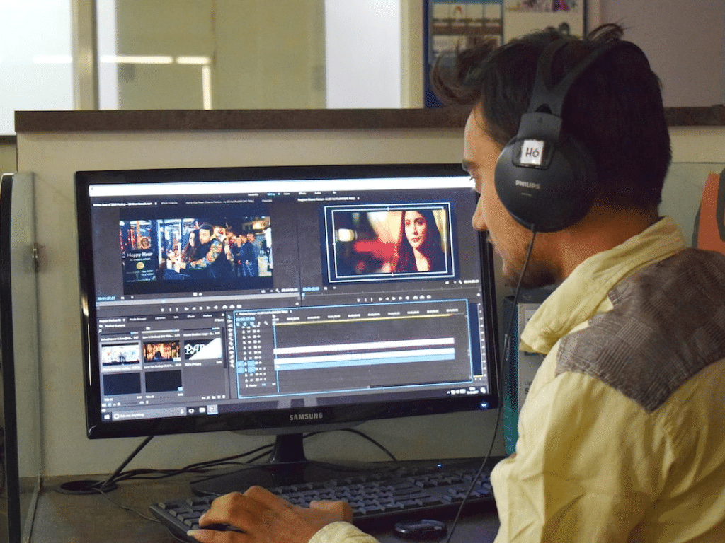 Une personne portant des écouteurs travaille sur un logiciel de montage vidéo sur un ordinateur de bureau. Le moniteur affiche plusieurs clips vidéo et chronologies d'édition.
