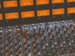 Close-up of an analog sound mixing console with multiple sliders and vu meters indicating levels.