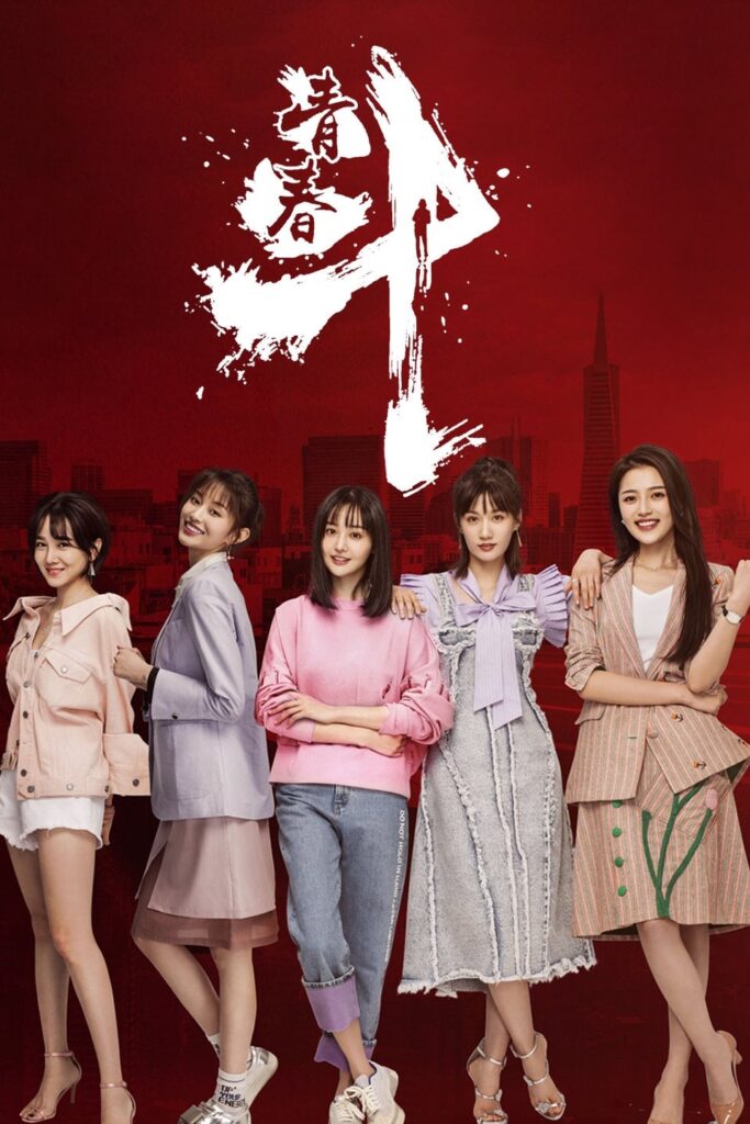 Cinq personnes se tiennent devant un fond rouge avec du texte blanc en haut. Le groupe comprend trois individus vêtus de tenues de couleur plus claire et deux en tenue légèrement plus foncée. Ils posent et sourient.