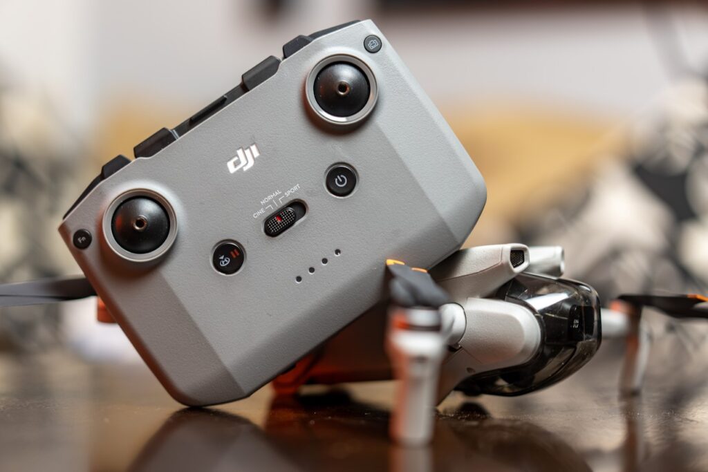 A drone controller rests on a folded drone, placed on a wooden surface with a blurred background, reminiscent of the careful setup in a dubbing studio.