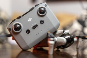 A drone controller rests on a folded drone, placed on a wooden surface with a blurred background, reminiscent of the careful setup in a dubbing studio.