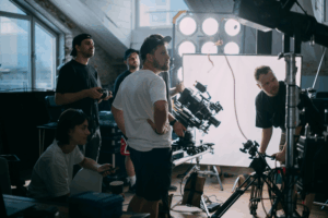 A film crew operates cameras and equipment on a set during a corporate video shoot, with multiple people focused on filming under bright studio lights.